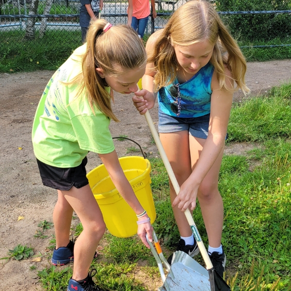 Zoo Camp children raking in goat habitat