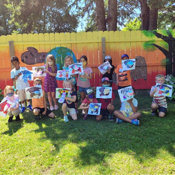 Group of smiling children hold up artwork