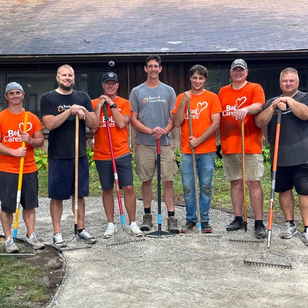 Group of smiling volunteers holding rakes stand on gravel pathway