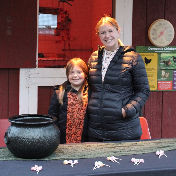 Smiling mother and daughter stand behind table with candy