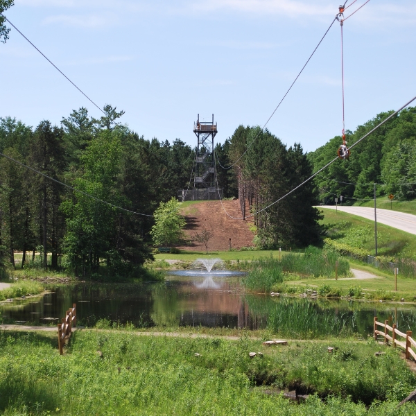 View of pond surrounded by green grass, with zipline tower in background