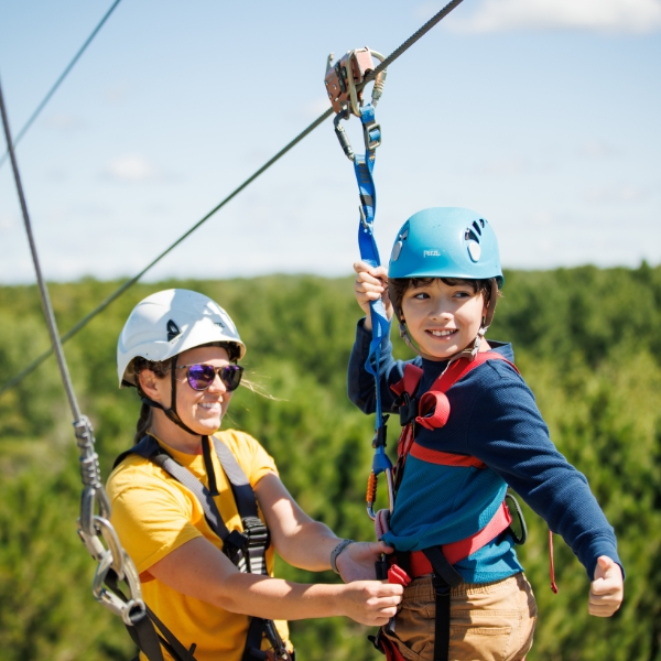 Guide helps boy get clipped into zip line at top of tower