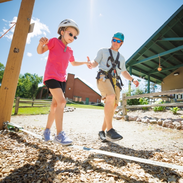 Girl balances on Kids Kourse with help from adult