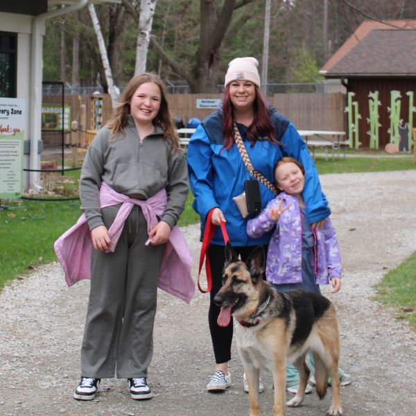 A mom and two daughters stand smiling with a german shepard on a leash.