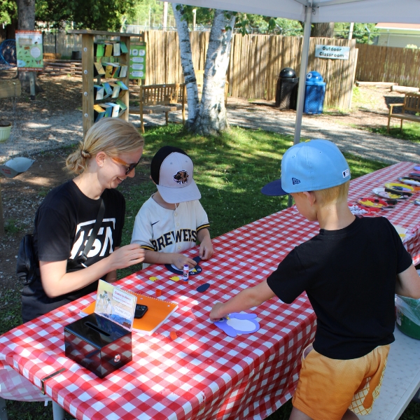 A mom and two boys sit at a craft table putting together a penguin paper puppet.