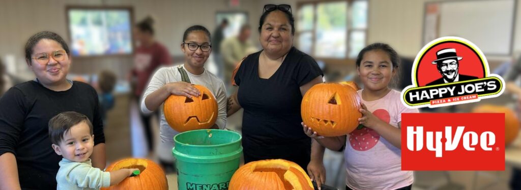 A family stands smiling while holding pumpkins they've carved