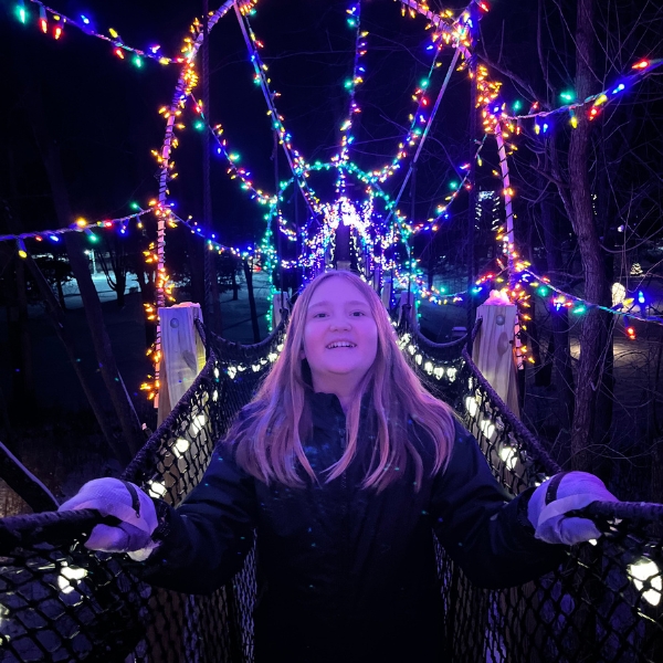 A girl stands, smiling, underneath the bright lights of the Canopy Tour