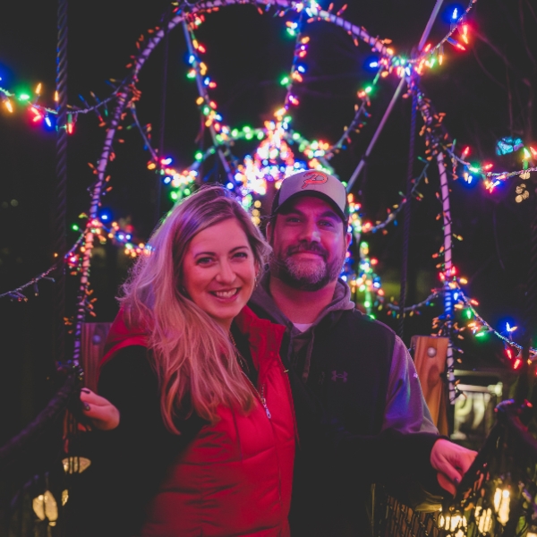 A man and woman stand together, smiling, underneath the colorful lights of the Canopy Tour