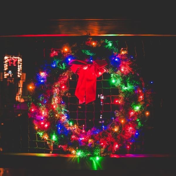 A wreath covered in bright holiday lights glows in the darkness.